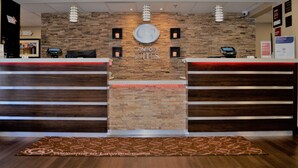 Una recepción con pared de piedra de fondo, un quiosco digital y un tapete de bienvenida.