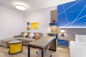 A modern hotel room with a sofa, a dining table, a yellow cabinet, a blue accent wall, and a ceiling light. - Comfort Suites Northside Hospital Gwinnett (Lawrenceville)