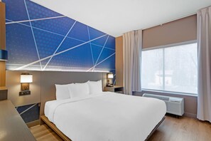 A hotel room with a large bed, a desk, a chair, a nightstand, a lamp, a telephone, a window with curtains, and a wall with a geometric pattern. - Comfort Suites Northside Hospital Gwinnett (Lawrenceville)