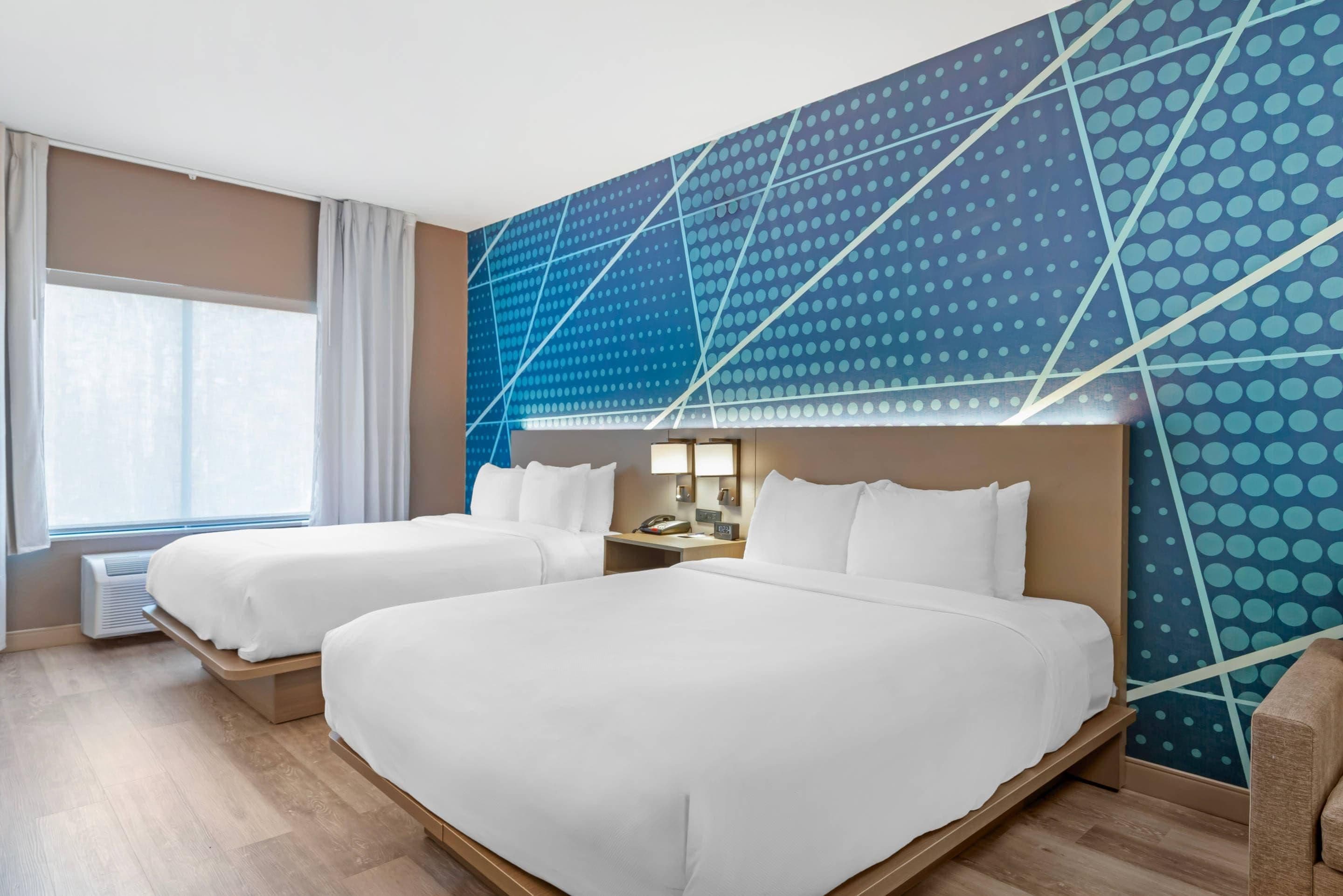 Une chambre d’hôtel avec deux lits, une grande fenêtre et un décor mural moderne.