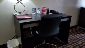 Habitación de hotel con escritorio, una silla, lámpara, basurero y teléfono instalado en la pared.