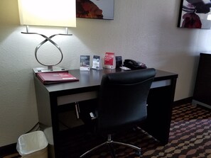 A hotel room with a desk, a chair, a lamp, a trash bin, and a wall-mounted telephone. - Comfort Suites Northside Hospital Gwinnett (Lawrenceville)