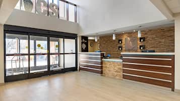 Un vestíbulo amplio con mostrador de recepción, una gran puerta de cristal de acceso y un techo alto con tragaluces.