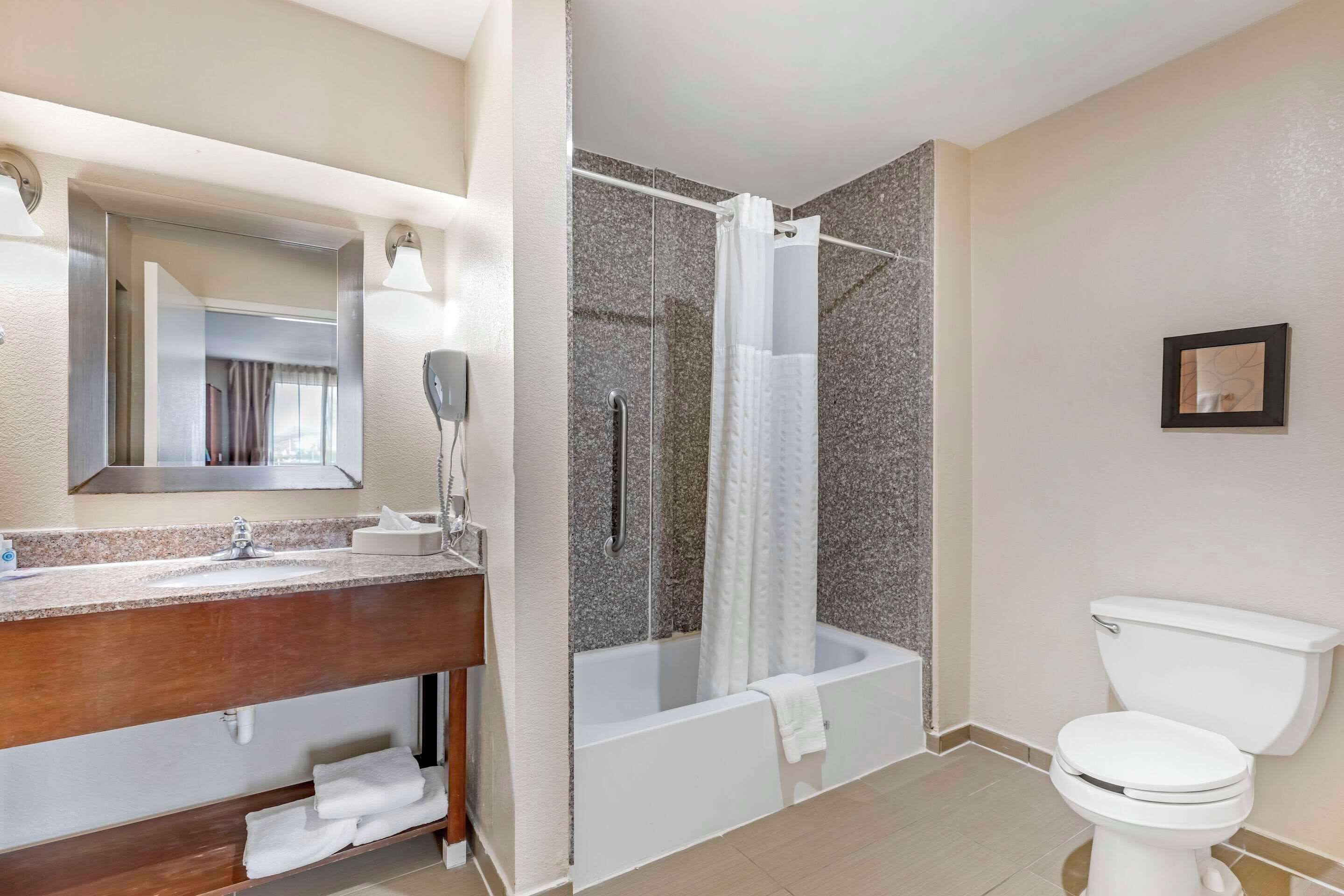 Un baño moderno con lavamanos de encimera de granito, un espejo, ducha con puerta de cristal y un inodoro blanco.
