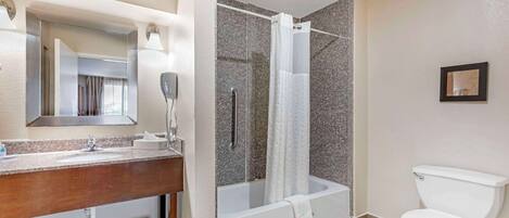 Un baño moderno con lavamanos de encimera de granito, un espejo, ducha con puerta de cristal y un inodoro blanco.