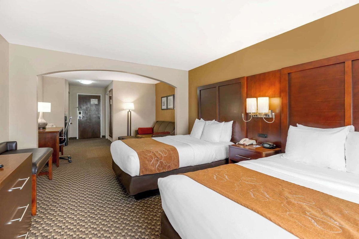 A hotel room with two beds, a desk, a chair, a lamp, and a phone on the nightstand.