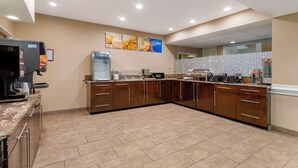 A modern kitchen with a coffee machine, water dispenser, and a large island with a sink. - Comfort Suites Port Allen - Baton Rouge (Port Allen)