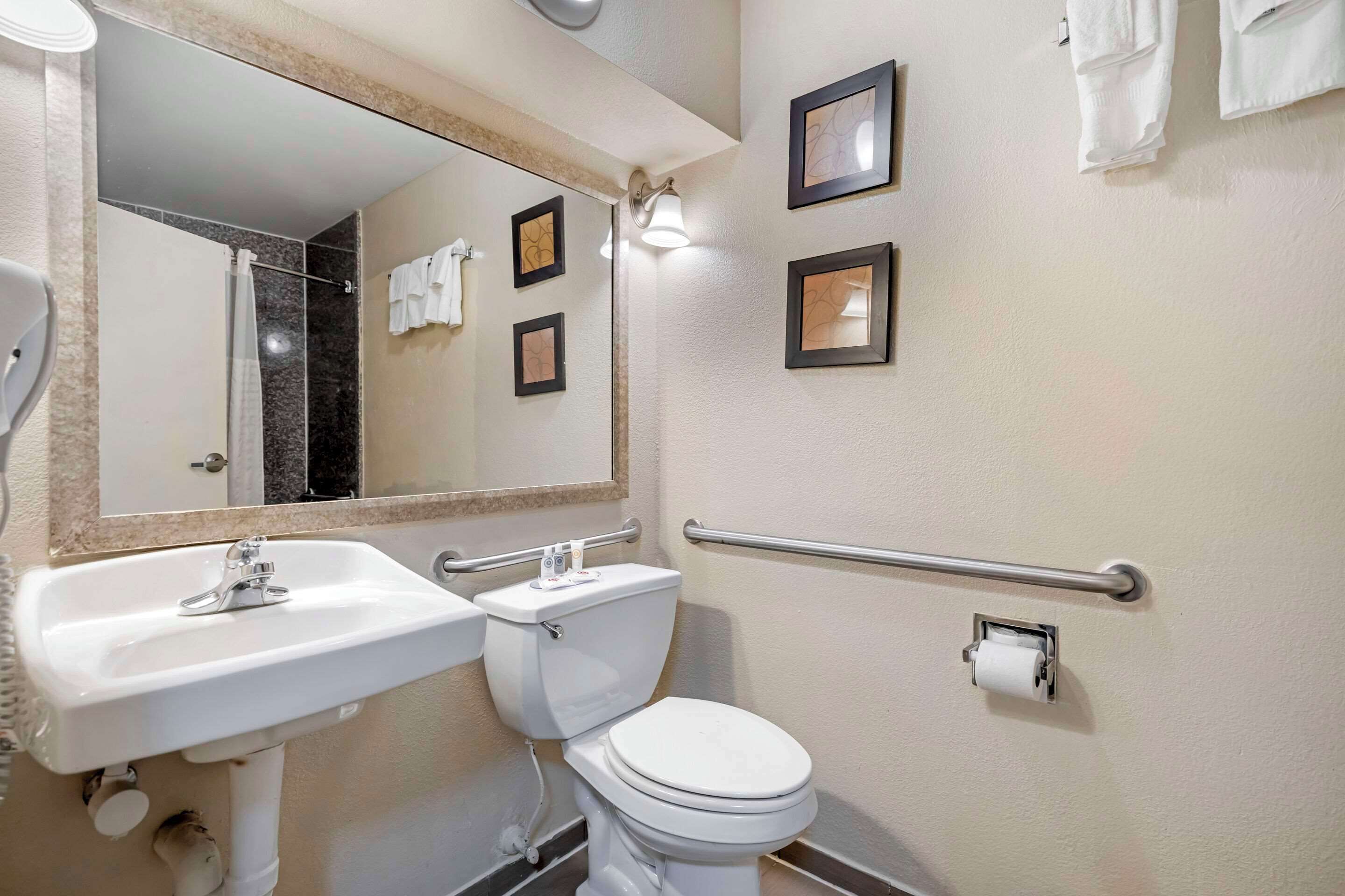 A bathroom with a white sink, toilet, and mirror. There are three framed pictures on the wall and a towel rack with towels.