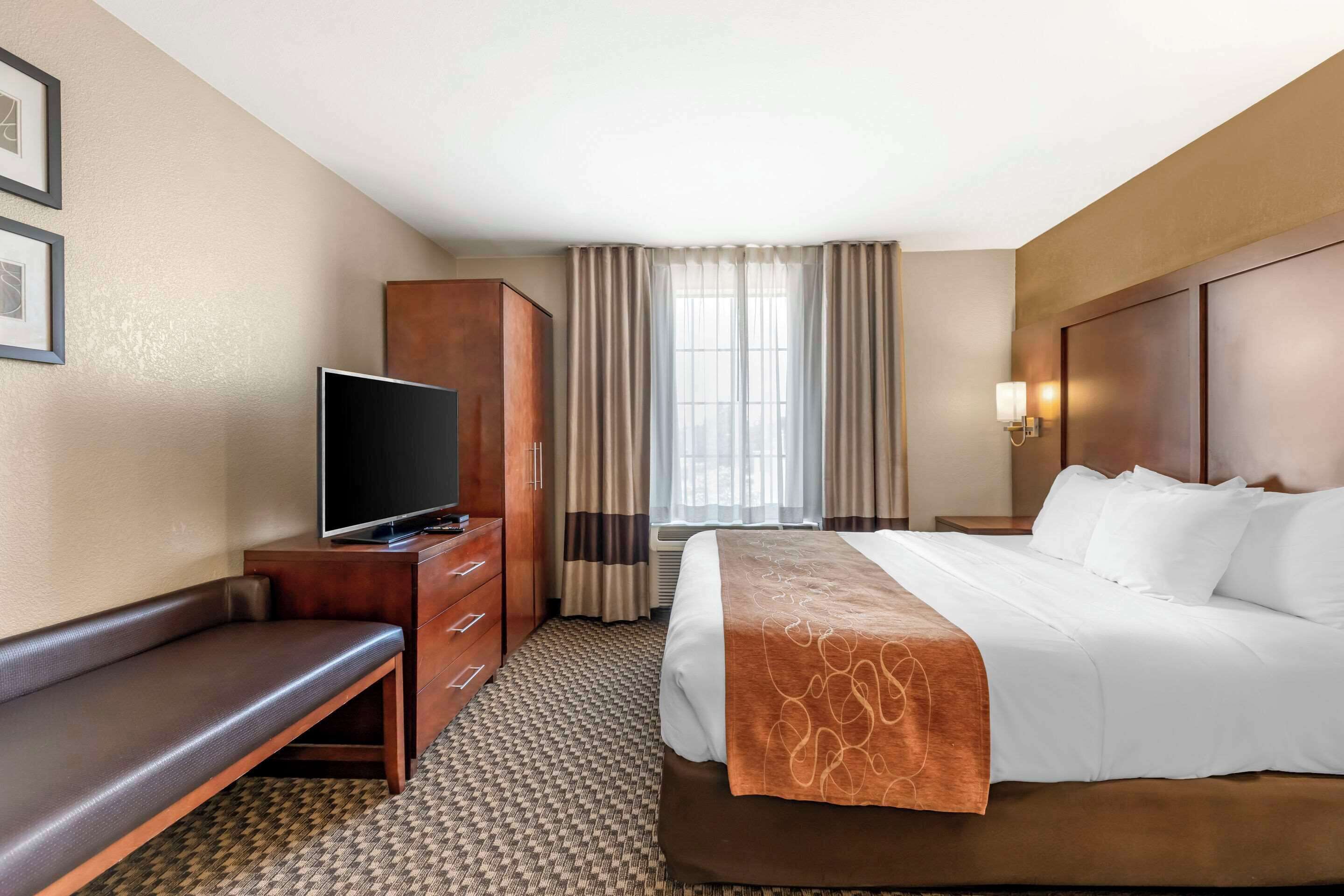 A hotel room with a bed, a TV, a bench, a wardrobe, and a window with curtains.