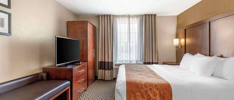 Quarto de hotel com cama, televisão, um banco, guarda-roupa e janela com cortinas.