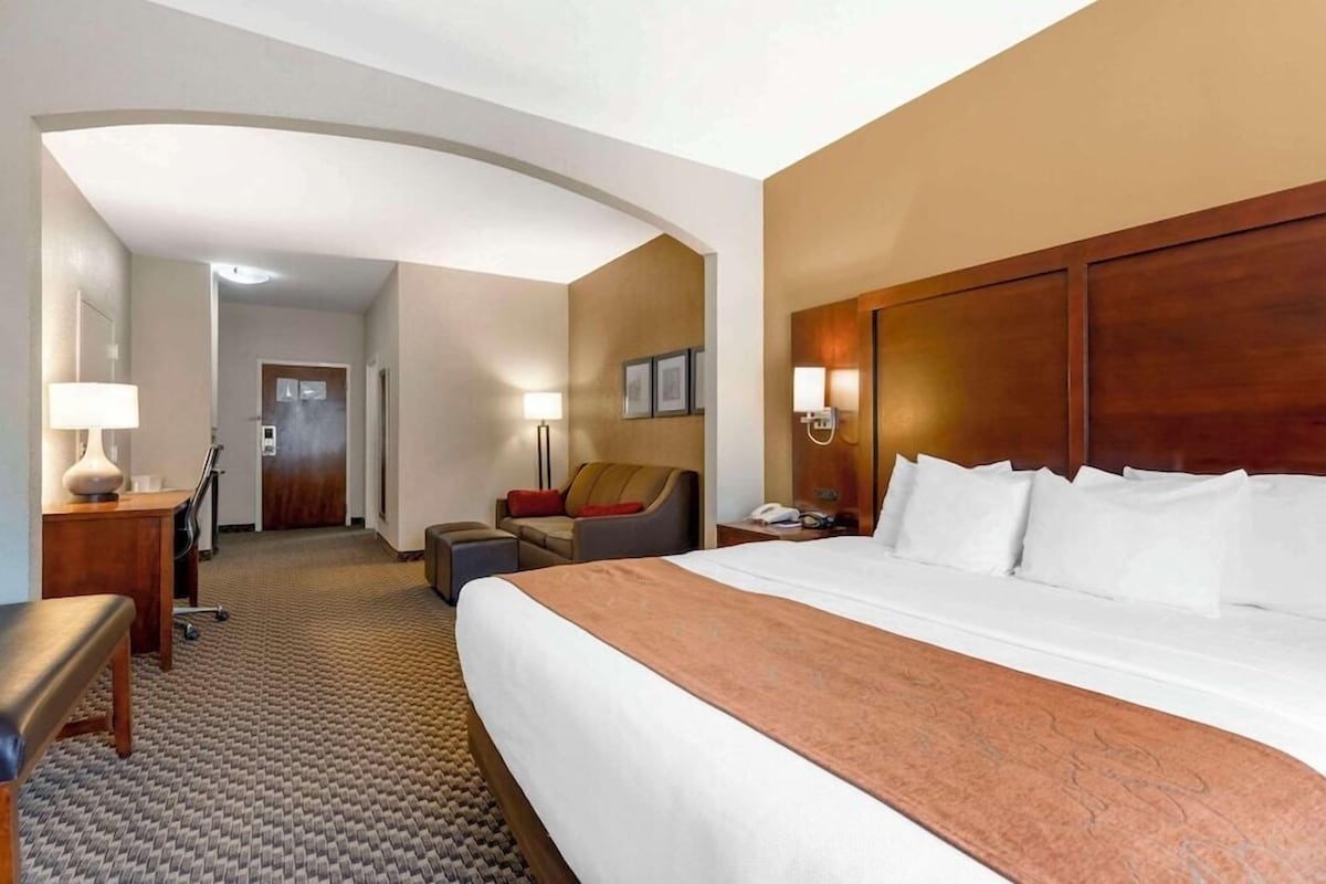 A hotel room with a large bed, a desk with a lamp, a chair, a sofa, and a small table with a phone.