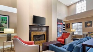 A hotel lobby with a fireplace, seating area, television, and vending machine. - Comfort Suites Port Allen - Baton Rouge (Port Allen)