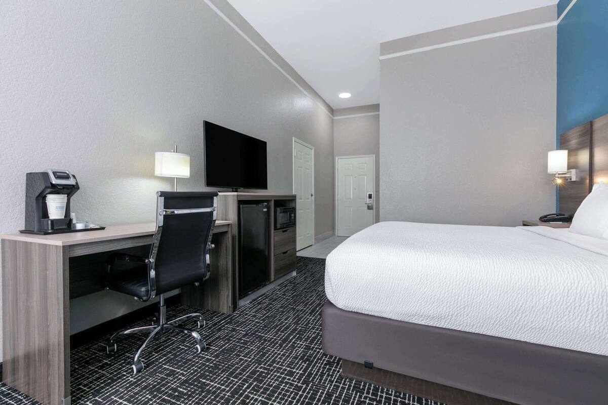 A hotel room with a bed, desk, chair, television, and a coffee machine.