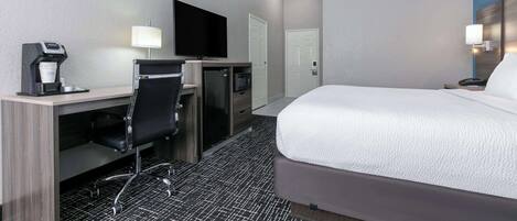 A hotel room with a bed, desk, chair, television, and a coffee machine.