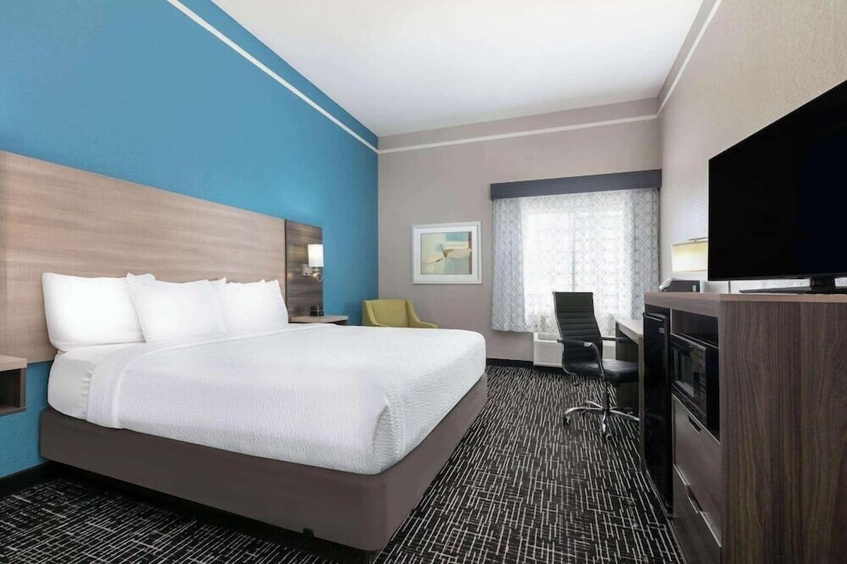 A hotel room with a large bed, a desk, a chair, a TV, and a window with curtains.