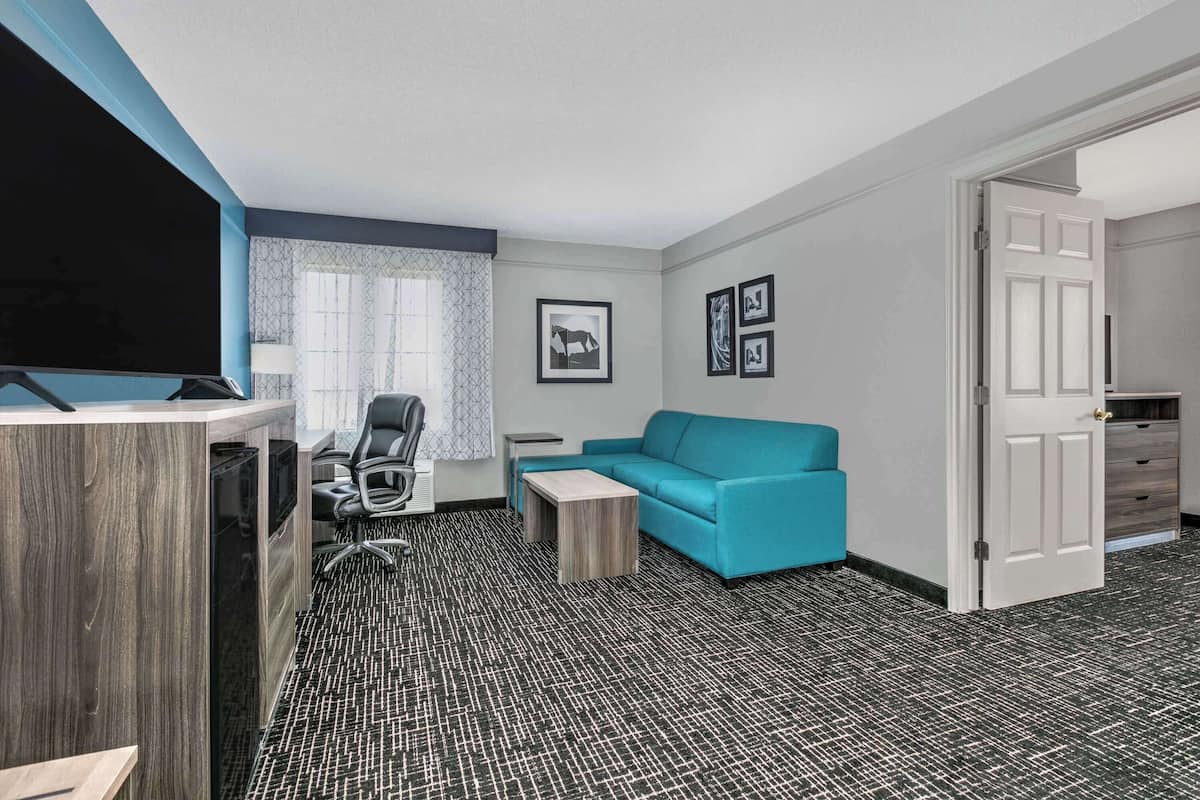 A modern hotel room with a desk, a blue sofa, a television, and a door leading to a bathroom.