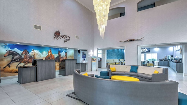 A spacious lobby with a modern reception desk, a large seating area with cushions, and a wall mural of horses. - La Quinta Inn & Suites by Wyndham Weatherford (Weatherford)