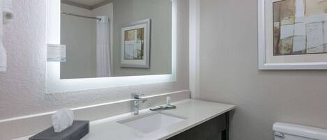 A bathroom with a white sink, a mirror, a framed artwork, and a toilet.