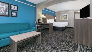 A hotel room with a blue wall, a bed, a desk, a chair, a television, and a coffee table. - La Quinta Inn & Suites by Wyndham Weatherford (Weatherford)