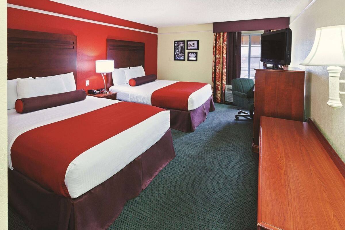 A hotel room with two beds, a desk, a TV, and a chair.