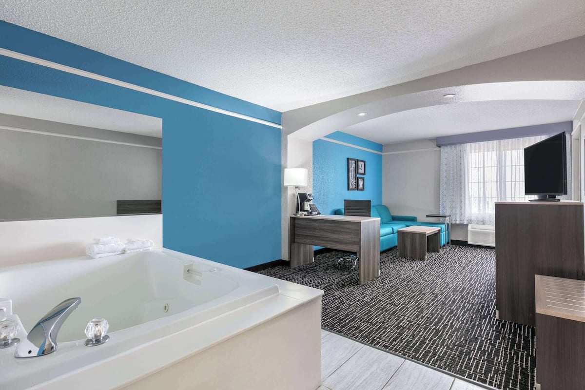 A modern hotel room with a large bathtub, a sofa, a desk, and a television.