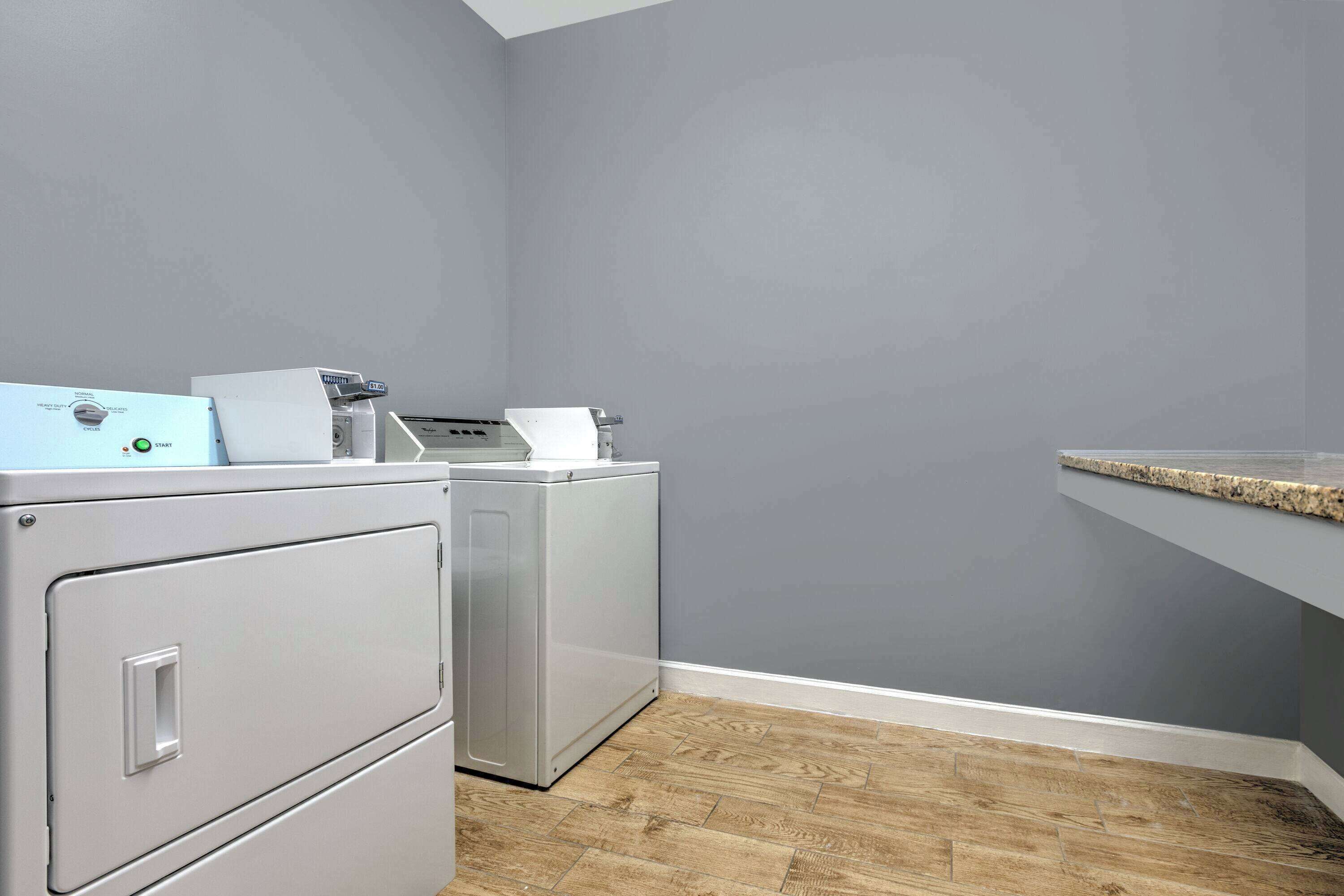 A laundry area with a washing machine and dryer, a countertop, and a wooden floor.