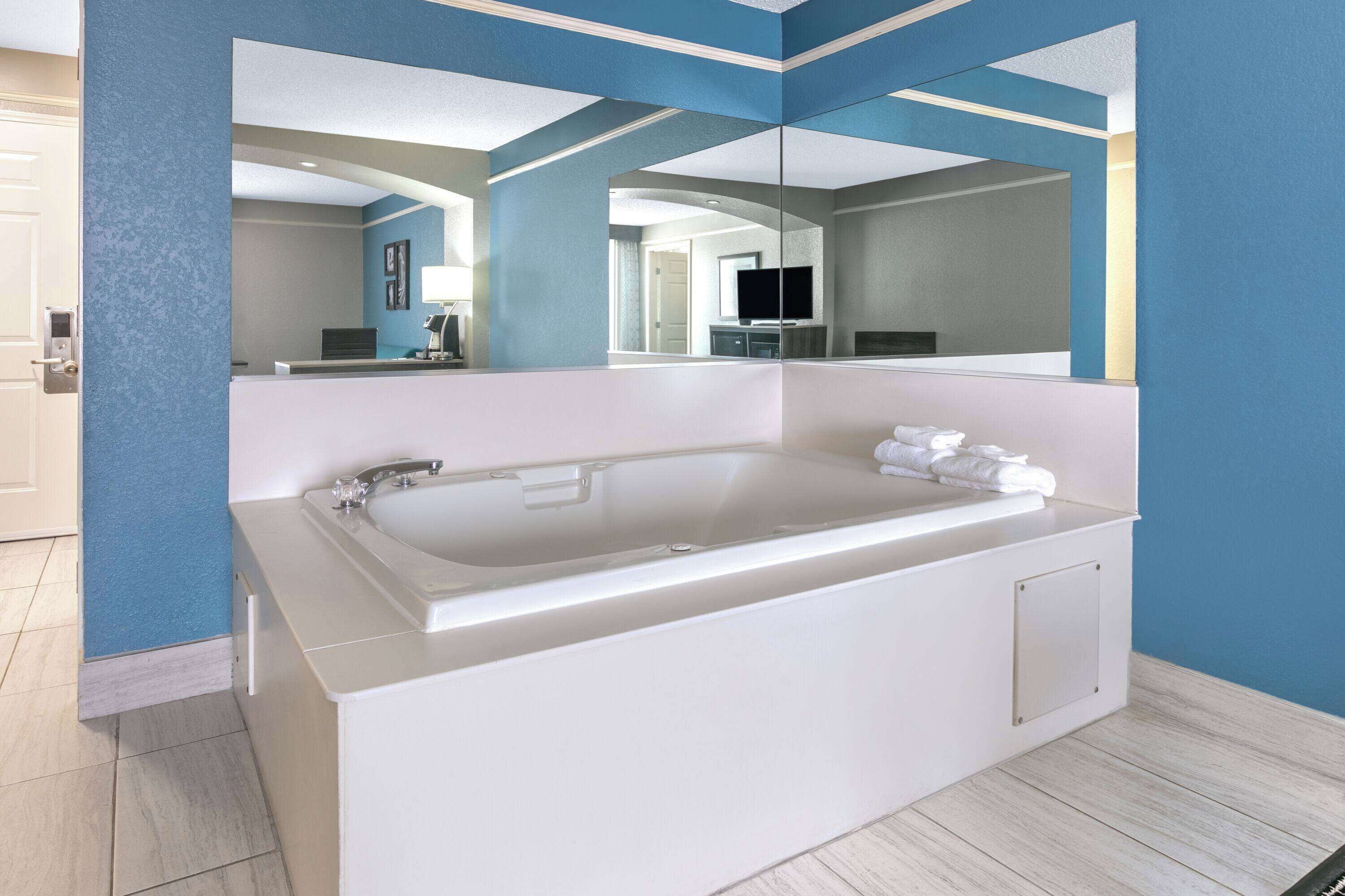 A modern bathroom with a large bathtub, a mirror, and a sink.