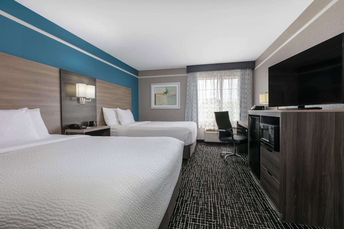 A hotel room with two beds, a TV, a desk with a chair, and a window with curtains.