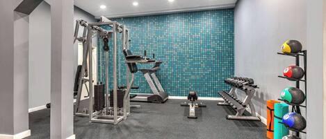 Ein Fitnessraum mit Trainingsgeräten, einer Wand mit blauem Muster und einem Medizinballständer.