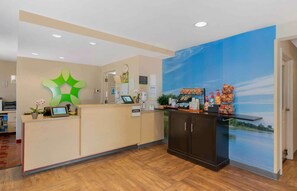 A reception area with a wooden floor, a reception desk, a wall-mounted clock, and a mural of a lake. - Extended Stay America Suites Newport News Yorktown (Yorktown)