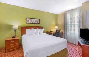 Habitación de hotel con cama, mesitas de noche, escritorio, silla, televisor y un cuadro en la pared.