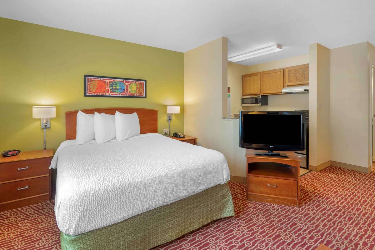 A hotel room with a bed, bedside lamps, a television, a microwave, and a kitchen area.