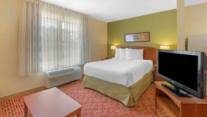 Habitación de hotel con cama, televisión de pantalla plana, calefacción, mesa y ventana con cortinas translúcidas.