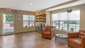Un vestíbulo espacioso con piso de madera, sillones de cuero, una mesa de centro y un refrigerador lleno de bebidas.
