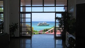 A spacious room with a large sliding glass door leading to a balcony with a view of the ocean and a boat.