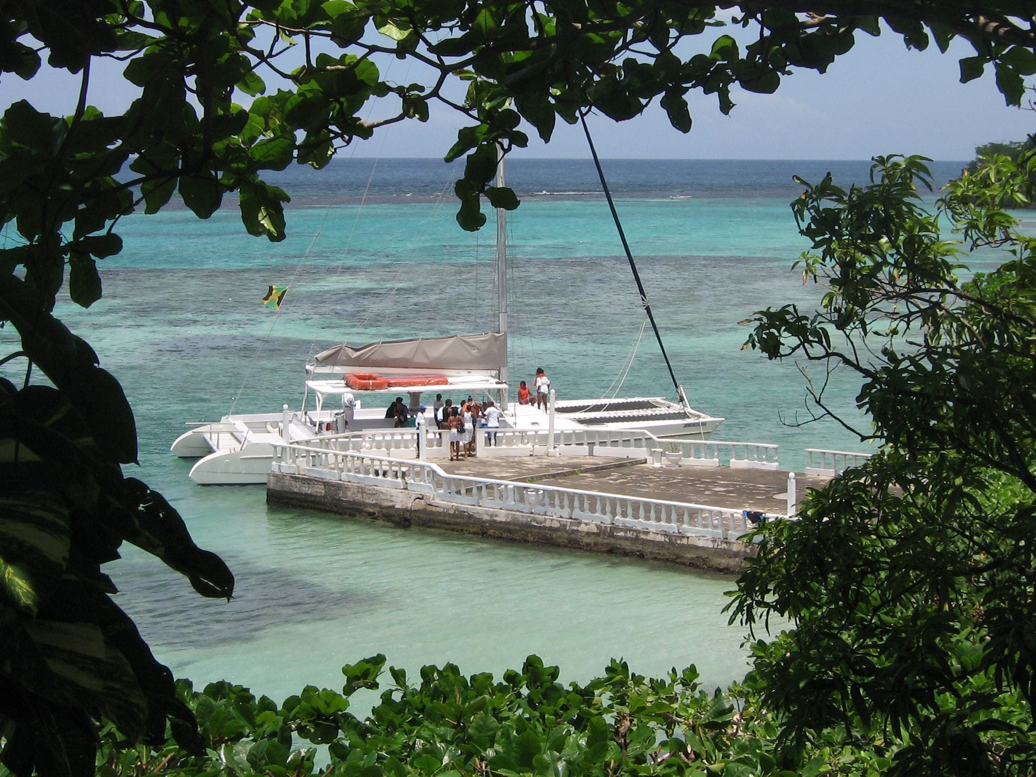 Eine Pier mit einem dort liegenden Boot, umgeben von klarem türkisblauem Wasser und üppiger Vegetation.