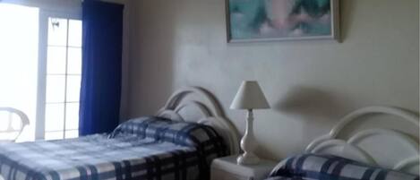 Un dormitorio con dos camas, una ventana con cortinas azules, un cuadro en la pared y una lámpara de noche.