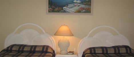 A bedroom with two beds, a nightstand with a lamp, and a painting of a coastal scene on the wall.