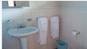 A bathroom with a sink, two towels hanging on a rack, a toilet paper holder, and a trash bin.