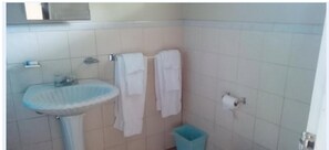A bathroom with a sink, two towels hanging on a rack, a toilet paper holder, and a trash bin.