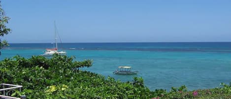 A coastal view with a clear blue sky, a red-roofed building, and a small boat in the water.