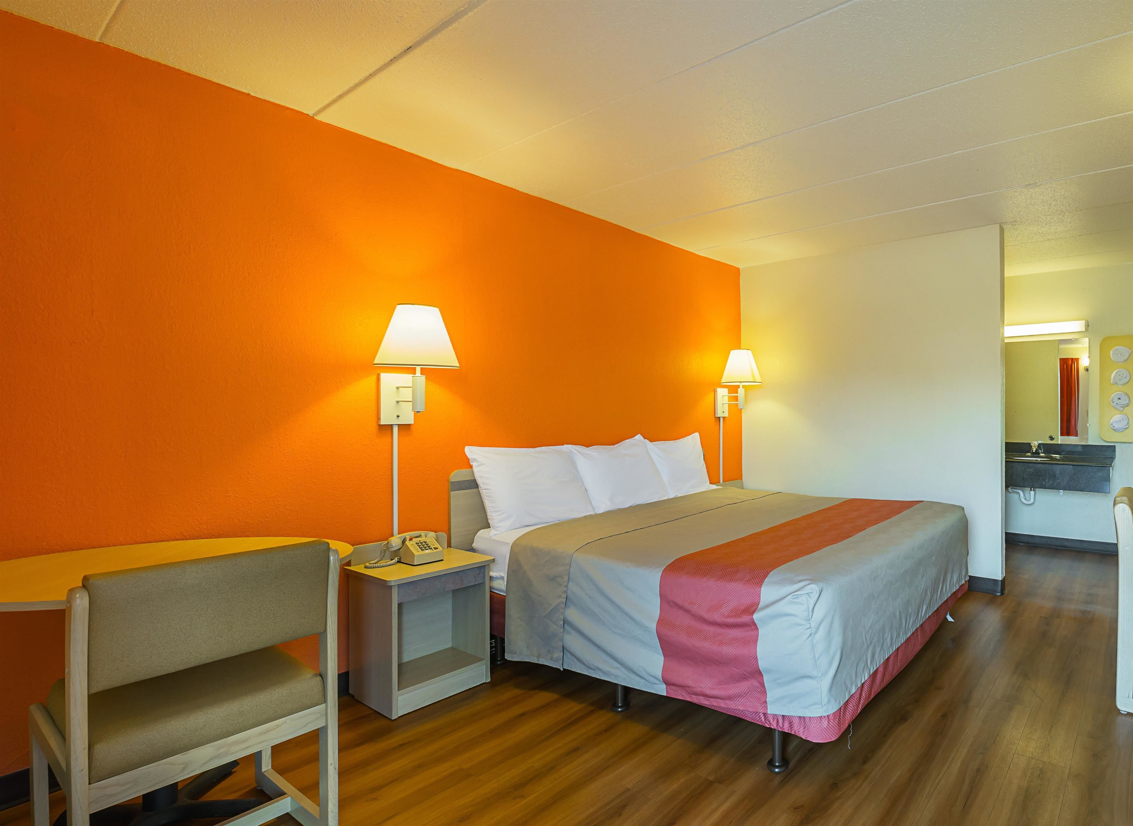 A hotel room with a bed, two bedside lamps, a desk with a chair, a telephone, and a bathroom visible through an open door.