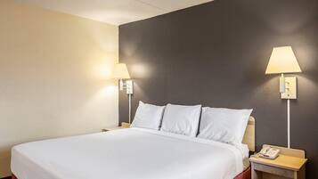 Een hotelkamer met een groot bed, twee bedlampen, een nachtkastje met een telefoon en een lichtschakelaar aan de muur.