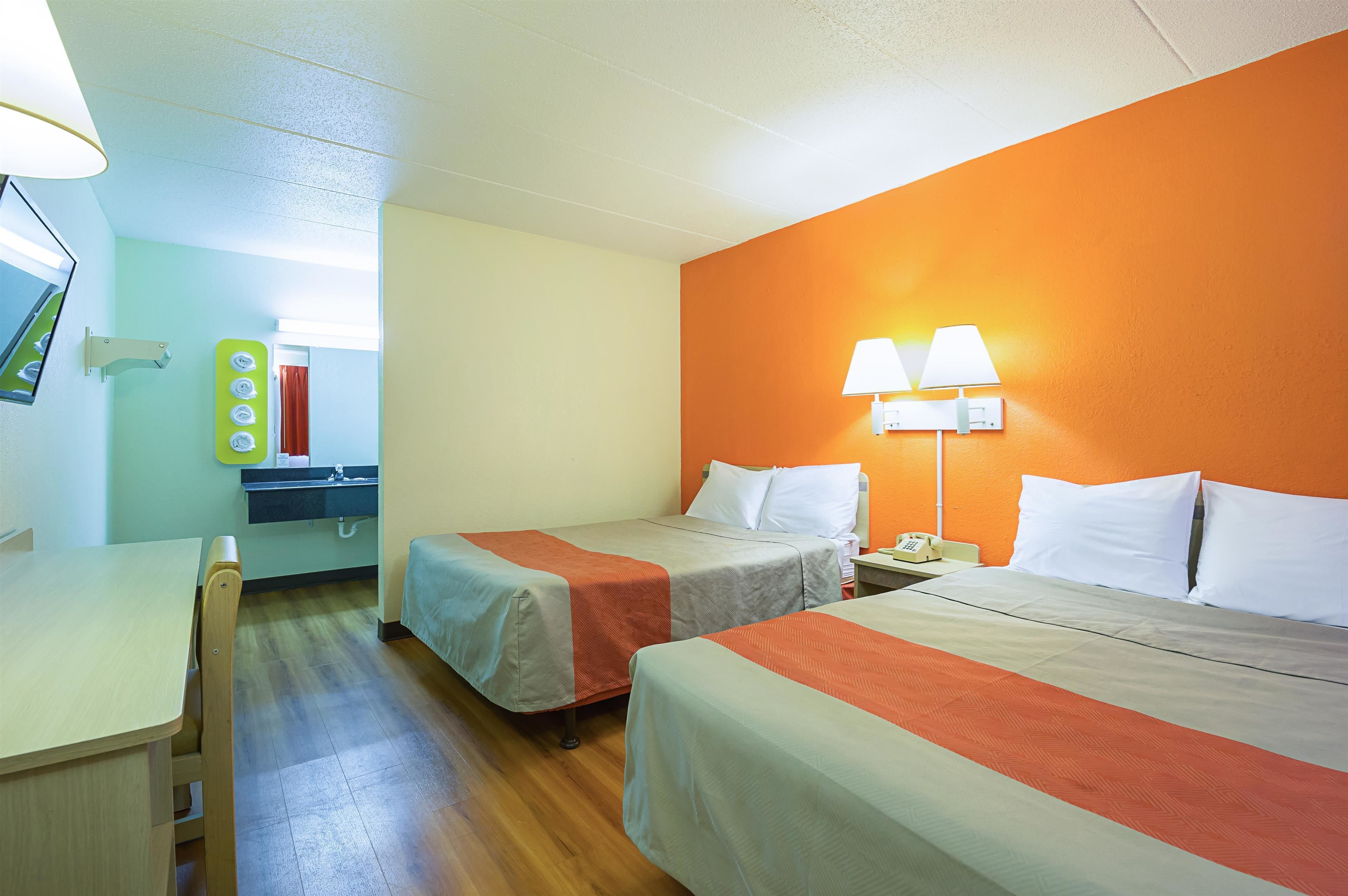 A hotel room with two beds, a desk, a mirror, and a window.