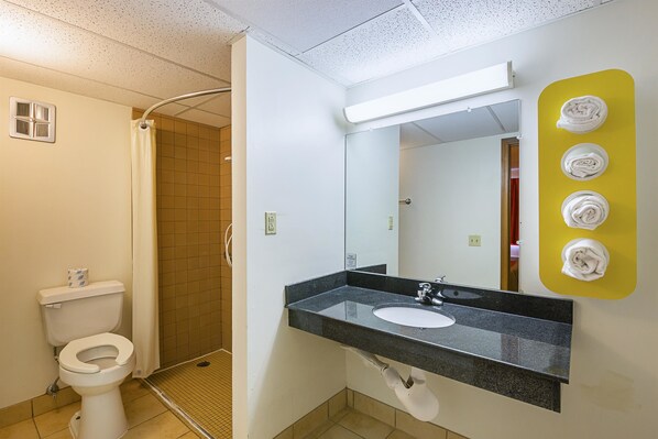 Et badeværelse med toilet, vask, spejl og bruser.