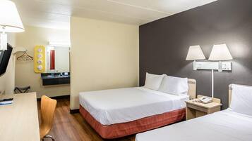 A hotel room with two beds, a desk, a chair, a mirror, a vanity with a sink, and two wall-mounted lamps.