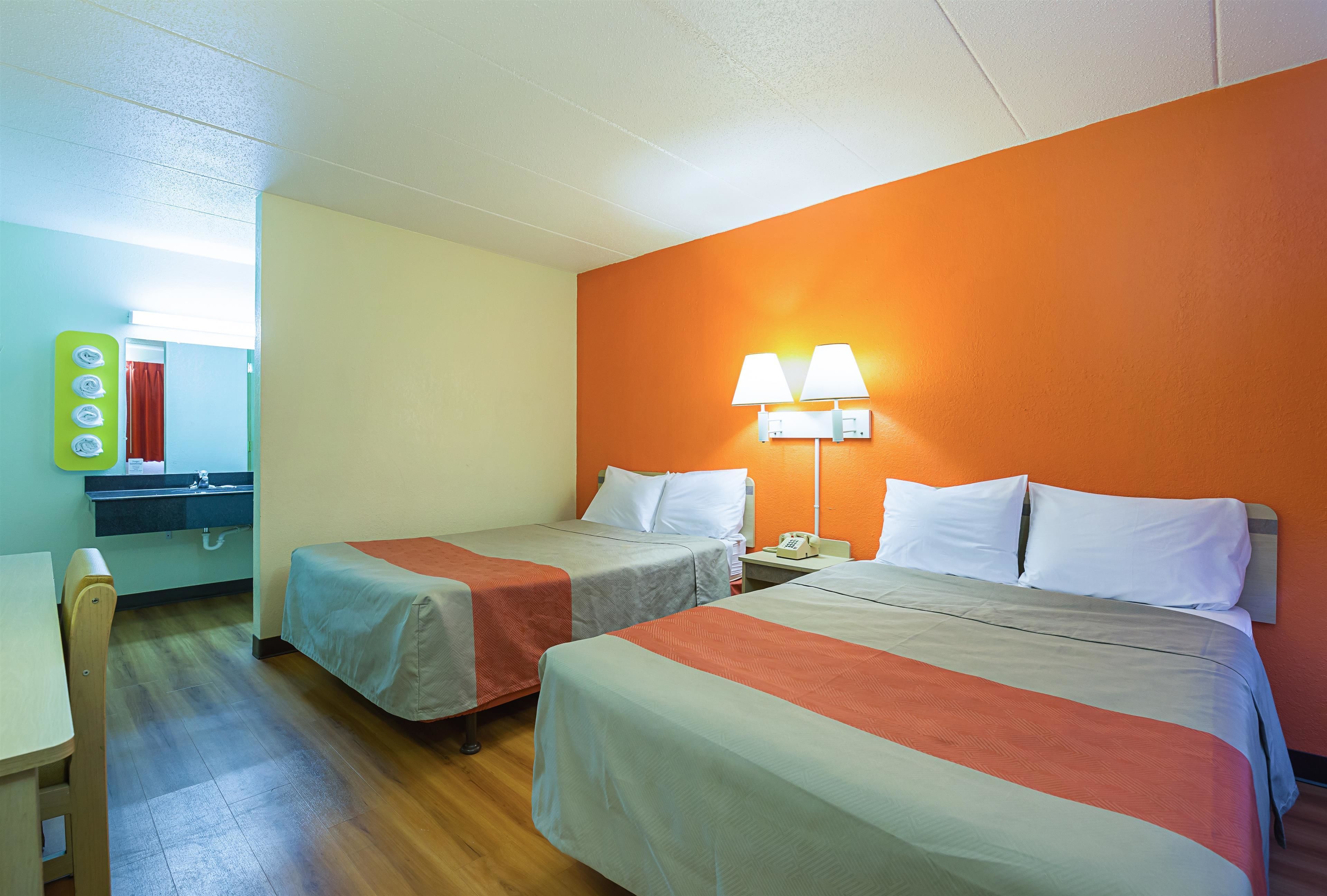 A hotel room with two beds, a desk, a chair, and a mirror.