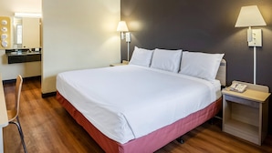 Une chambre d’hôtel avec un grand lit, une table de chevet avec une lampe, une chaise et une petite table avec un téléphone.