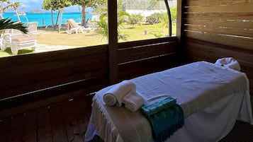 Relax in this serene room with a comfortable bed, a large window offering a beach view, and a wooden floor.