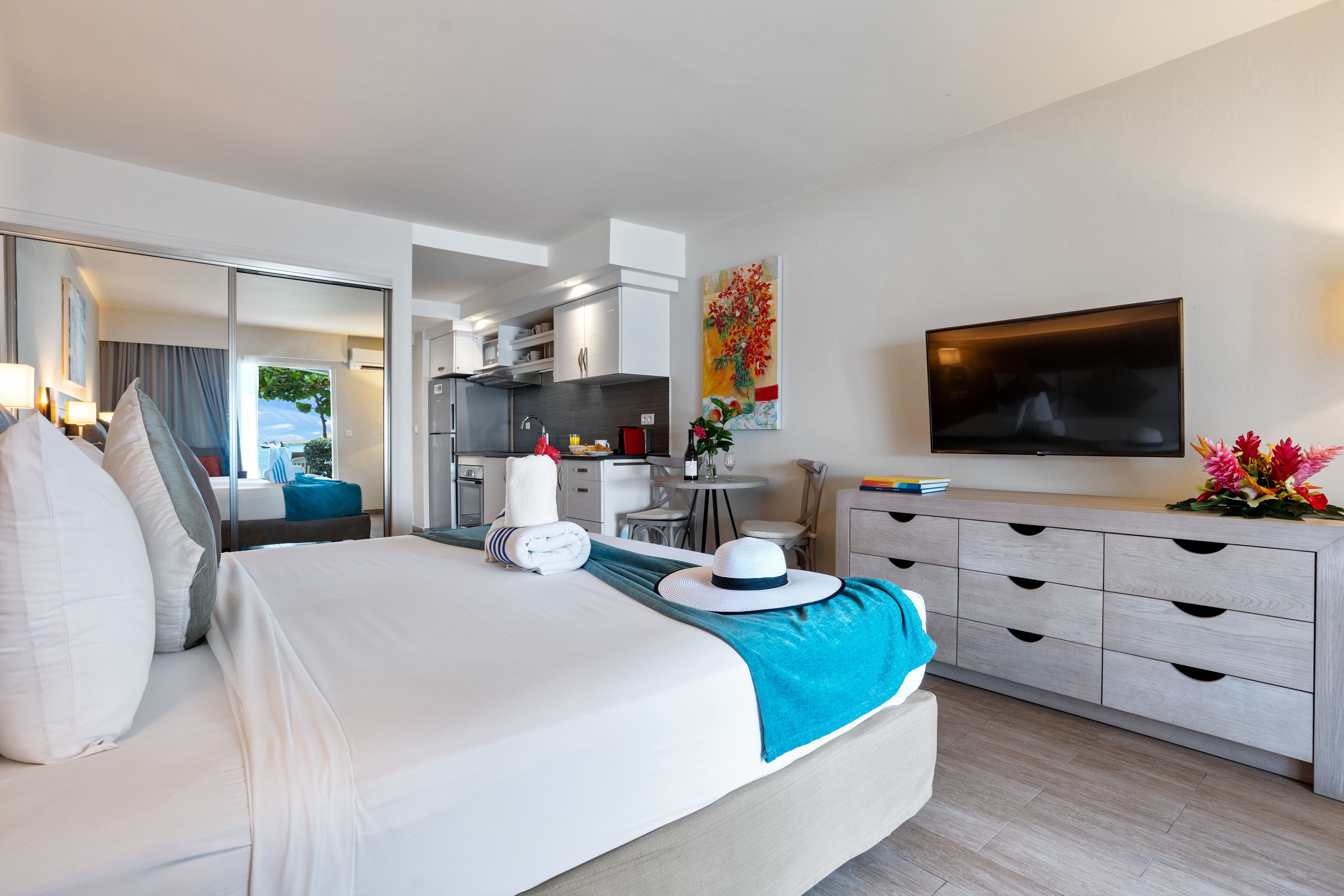 Quarto de hotel moderno com uma cama grande, área de refeições, cozinha e TV na parede.